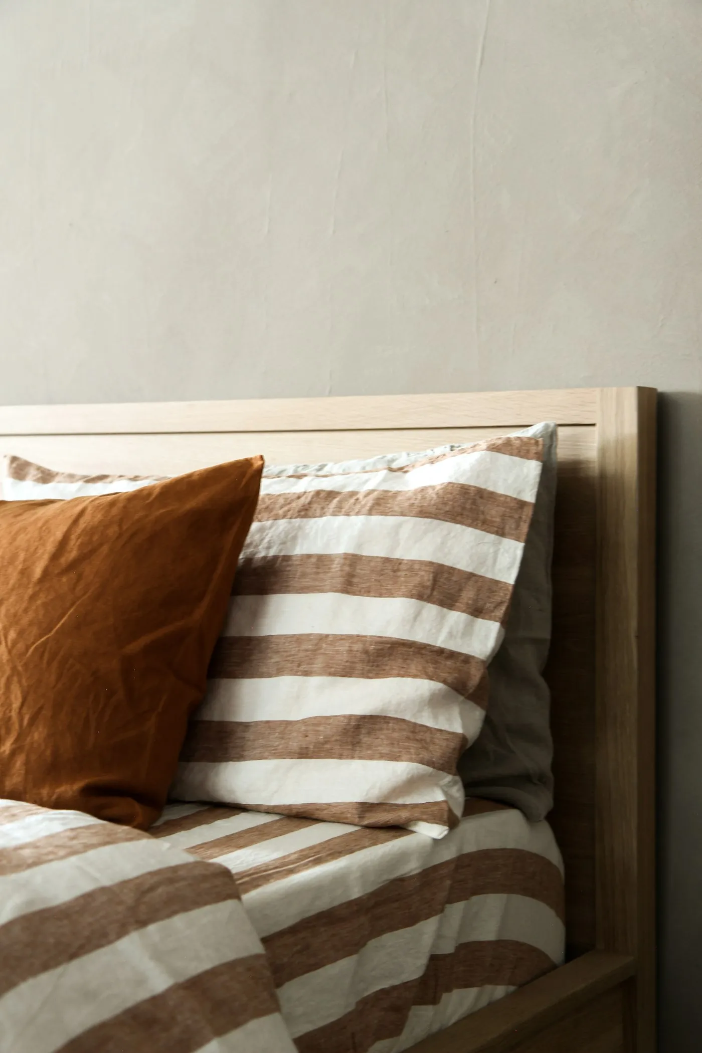 Terracotta and striped linen bedding against a light oak headboard